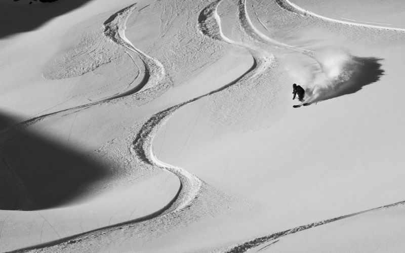 heli-skiing-skier-going-down-a-slope-with-tracks-through-the-snow-min