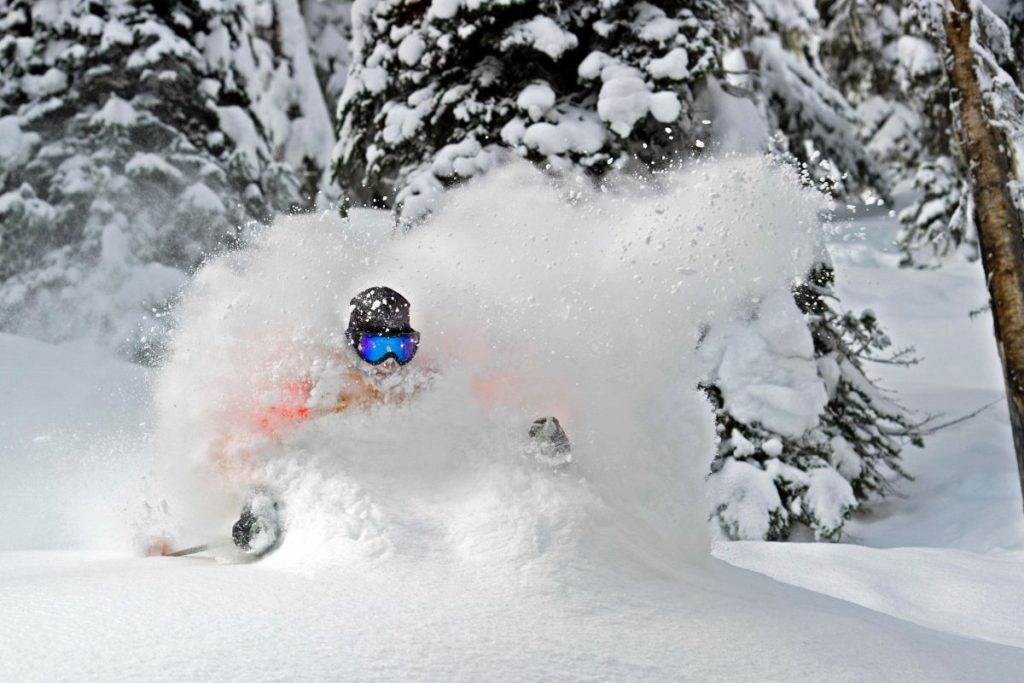 heli-skiing-skier-running-through-deep-powdered-snow-min