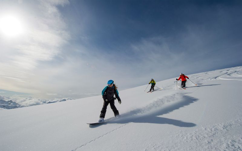 helicopter-skiing-three-skiers-carving-through-the-snow-min