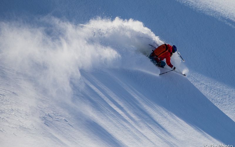 heli-skiing-skier-mkaing-sharp-turn-through-light-powder-min