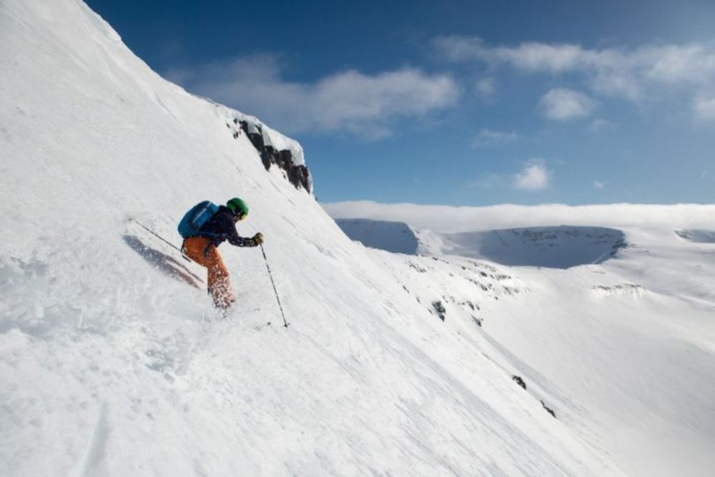 helicopter-skiing-heading-down-slope-with-mountain-ranges-in-background-min